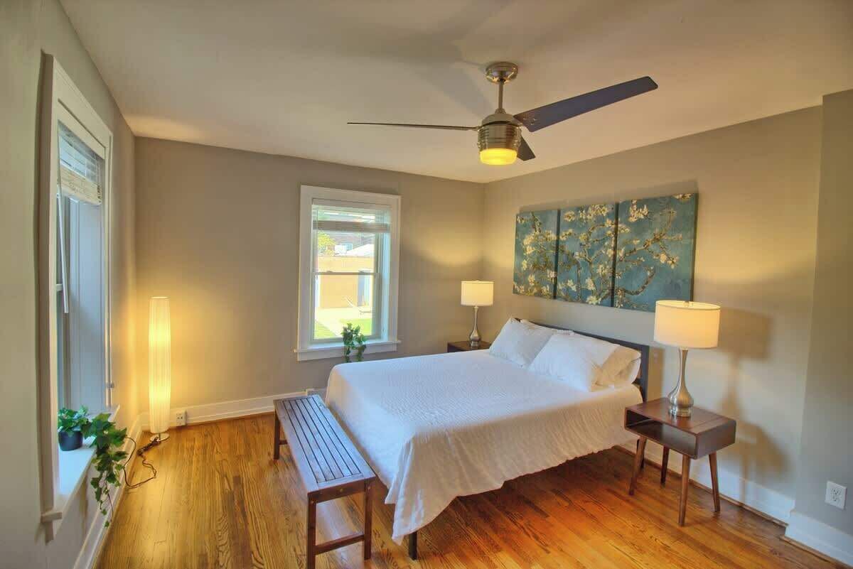 A bedroom with a bed, bedside tables, a ceiling fan, a window, and a wall-mounted artwork.