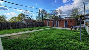 A backyard with a wooden fence, a brick building with doors, and a grassy area.