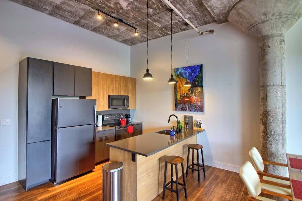A modern kitchen with a central island, stainless steel appliances, pendant lighting, and a painting on the wall.