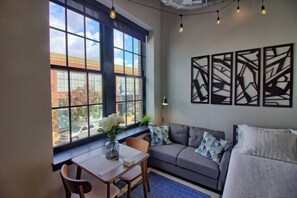 A modern room with a large window, a sofa, a table with chairs, and abstract wall art.