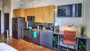 A modern kitchen with wooden cabinets, stainless steel appliances, and a bar stool. - Chic Ultramodern Studio Loft w/ Designer Features (Saint Louis)