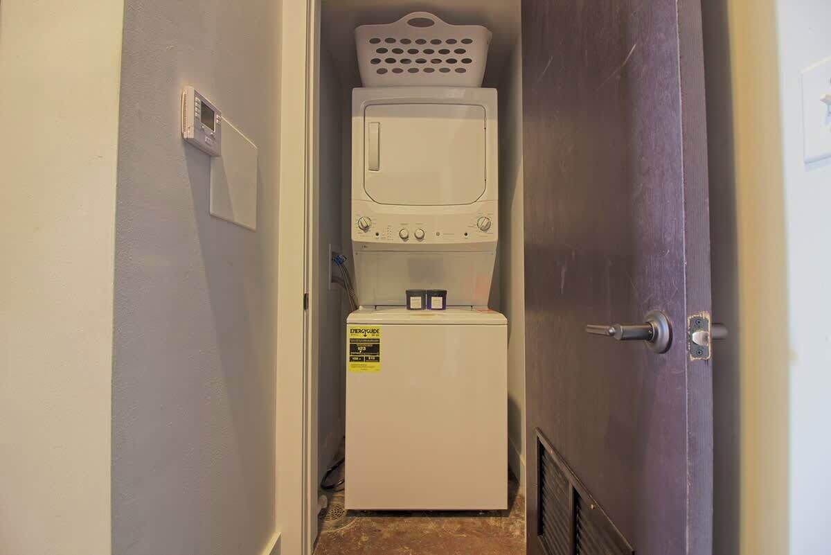 Un cuarto de lavandería con lavadora y secadora, una cesta encima de la secadora, y una puerta con manija.