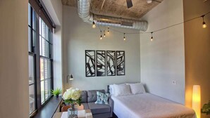 A modern hotel room with a large bed, a sofa, a dining table, and a view through large windows. - Chic Ultramodern Studio Loft w/ Designer Features (Saint Louis)