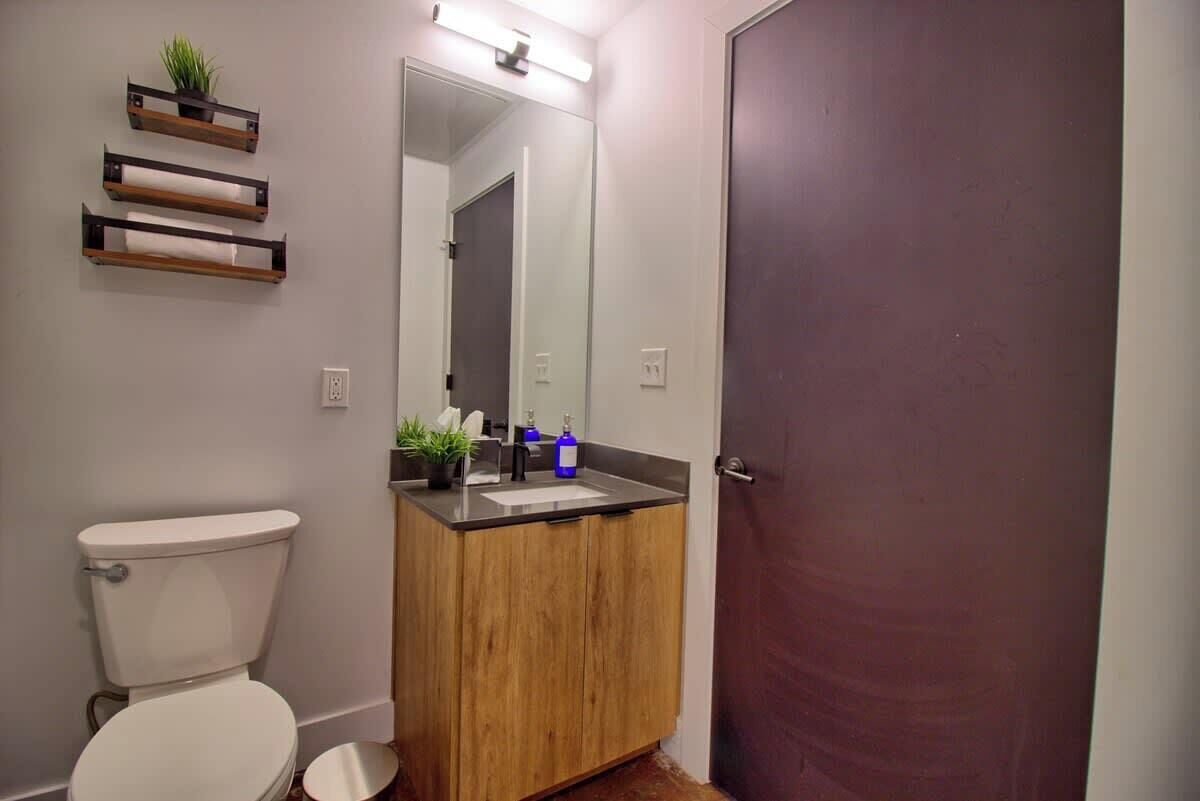 Ein Badezimmer mit Toilette, Holzwaschtisch, Waschbecken, Spiegel und drei Pflanzenregalen.