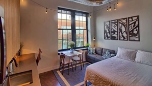 A room with a bed, a desk, a chair, a window, and abstract wall art. - Chic Ultramodern Studio Loft w/ Designer Features (Saint Louis)