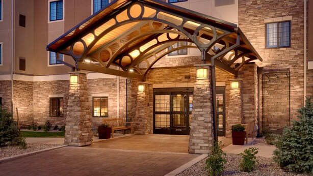 A hotel entrance with a covered patio, stone facade, and a bench. - 1 Bedroom | Fully Equipped Suite + Wi-Fi! (Cheyenne)