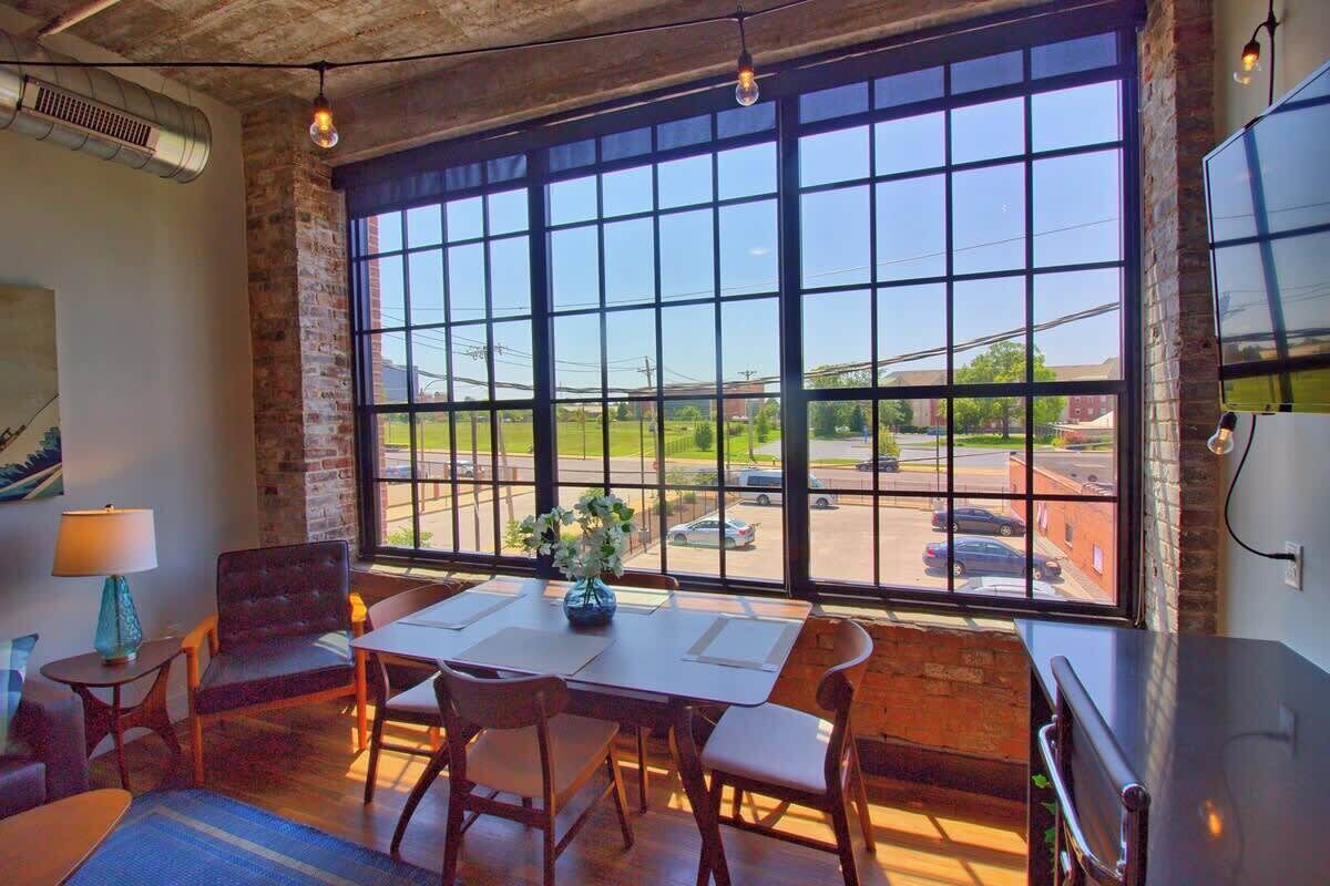 A room with a large window, a table with chairs, a lamp, and a plant.
