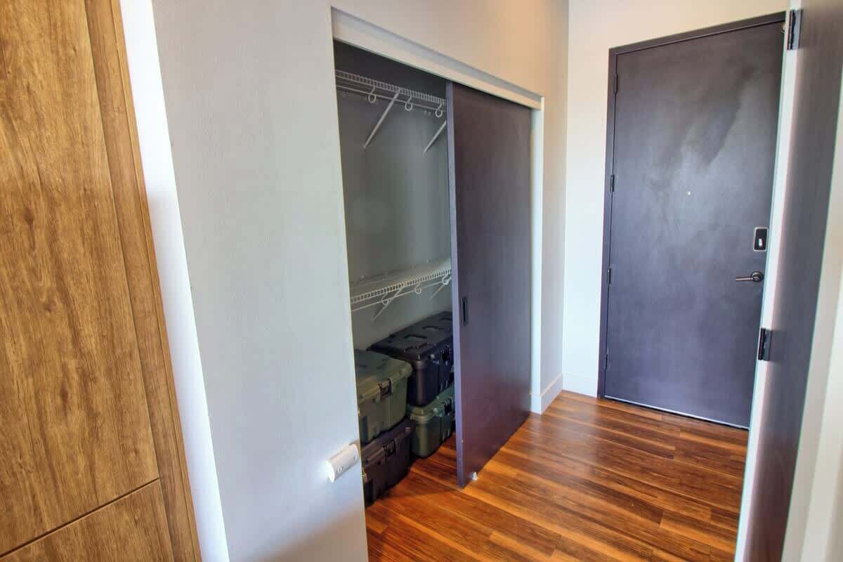 A hallway with a wooden floor, a closet with hanging storage, and a closed door.