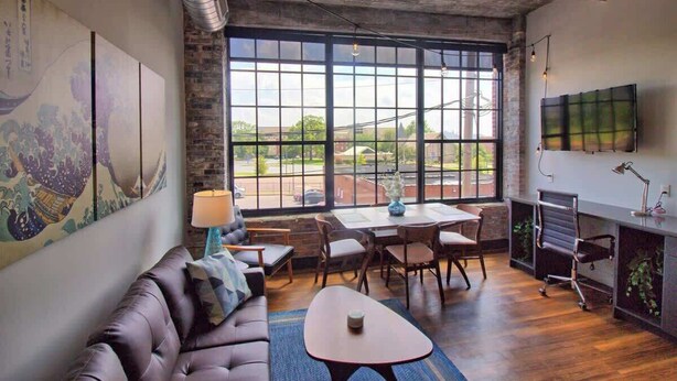 A modern interior with a leather sofa, dining table, chairs, and a large window offering a view of the outside. - Chic Ultramodern Studio Loft w/ Designer Features (Saint Louis)