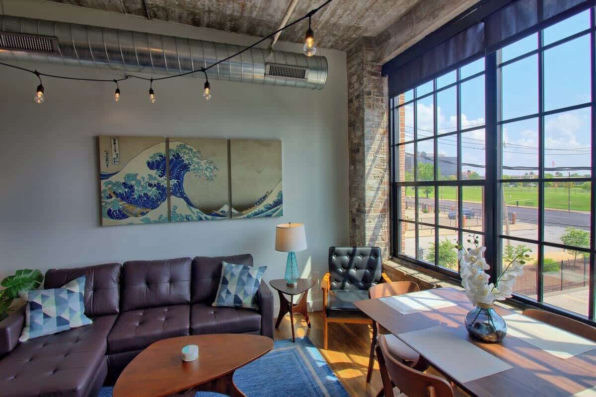 Un salon moderne avec un canapé, une table basse et une table à manger avec des chaises. Une grande fenêtre offre une vue sur l’extérieur.