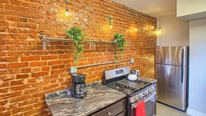 A kitchen with a brick wall, stainless steel appliances, and hanging plants. - Irises at TG Park | Fenced Backyard+W/D+Storage (Saint Louis)
