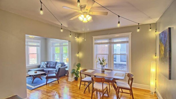 A spacious living area with a dining table, chairs, a sofa, and a ceiling fan. - Irises at TG Park | Fenced Backyard+W/D+Storage (Saint Louis)