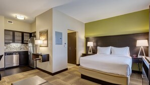 A hotel room with a bed, bedside tables, a desk, a kitchenette, and a bathroom. - Studio | Lovely Suite Close to Edward Jones! (Maryland Heights)