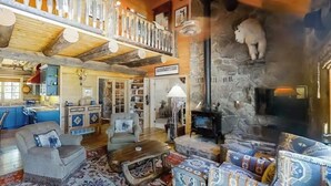 Un interior rústico con chimenea de piedra, vigas de madera y un balcón.