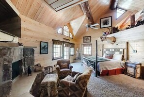 L’intérieur d’une cabane en rondins, avec une cheminée, des murs en bois, un lit, une chaise et un ventilateur de plafond.