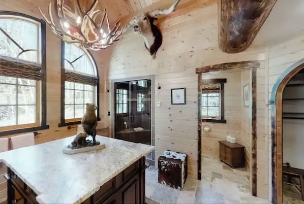 A rustic interior with wooden walls, a large deer head mounted on the ceiling, and a small statue on the counter. - Private Mountain Estate 🌲🏔️ 🌻 (Tabernash)