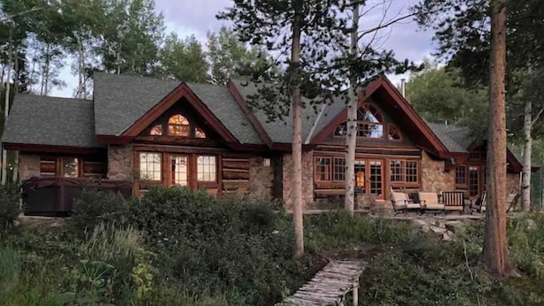 Una cabaña de madera con base de piedra, revestimiento de madera y un porche cubierto con mobiliario exterior.
