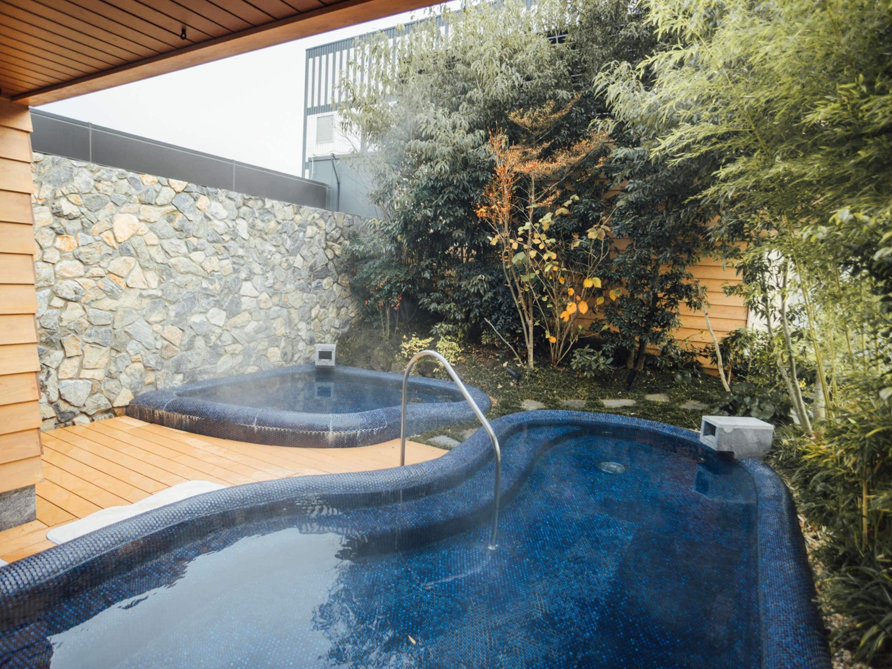 A hot tub with a stone wall and wooden deck, surrounded by greenery.