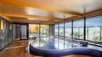 Ein moderner, überdachter Schwimmbereich mit geschwungenem Design, großen Fenstern mit Seeblick und einer Holzbalkendecke.