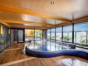 A modern indoor swimming pool with a curved design, large windows offering a view of a lake, and a wooden ceiling. - Mercure Hida Takayama (Takayama)