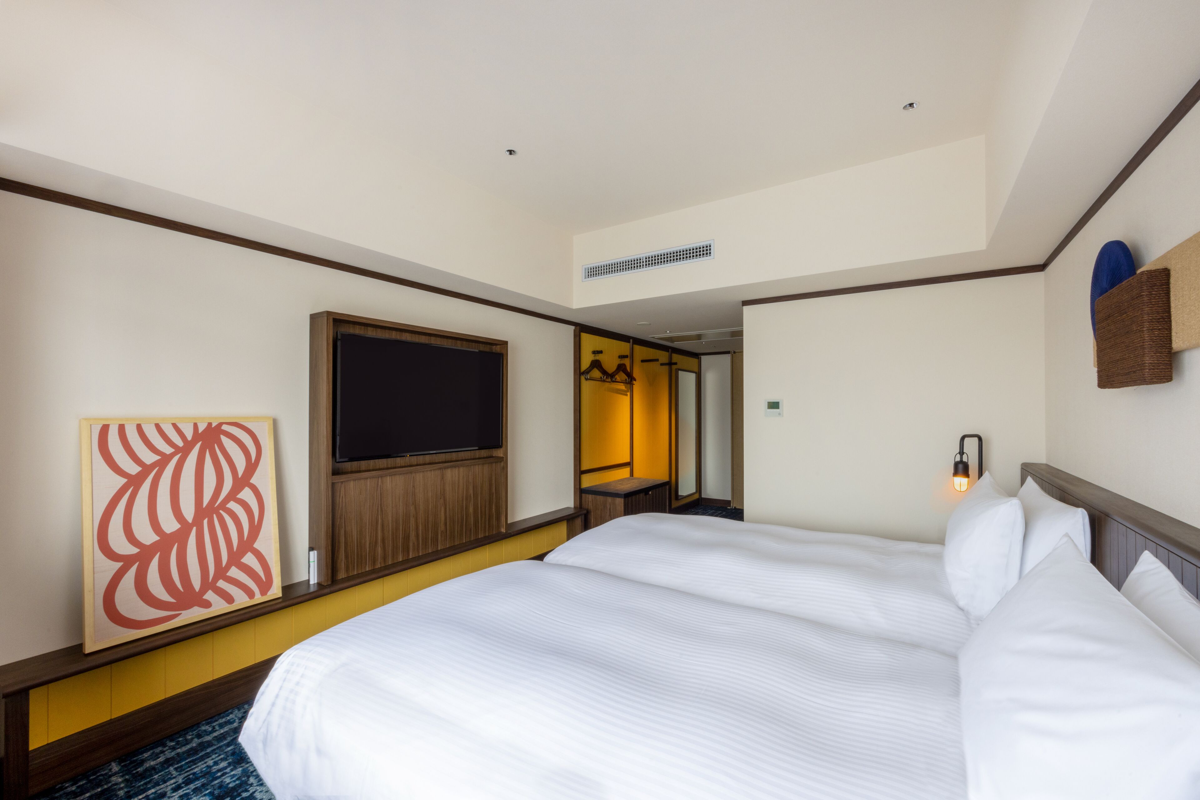 Una habitación de hotel con una cama grande, un televisor de pantalla plana, una obra de arte colgada en la pared y una pequeña zona de estar con una mesa y sillas.