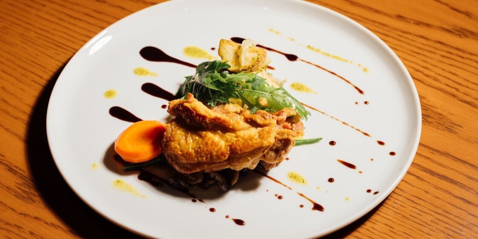 A white plate with a piece of fried chicken, a carrot, and greens on a wooden table.