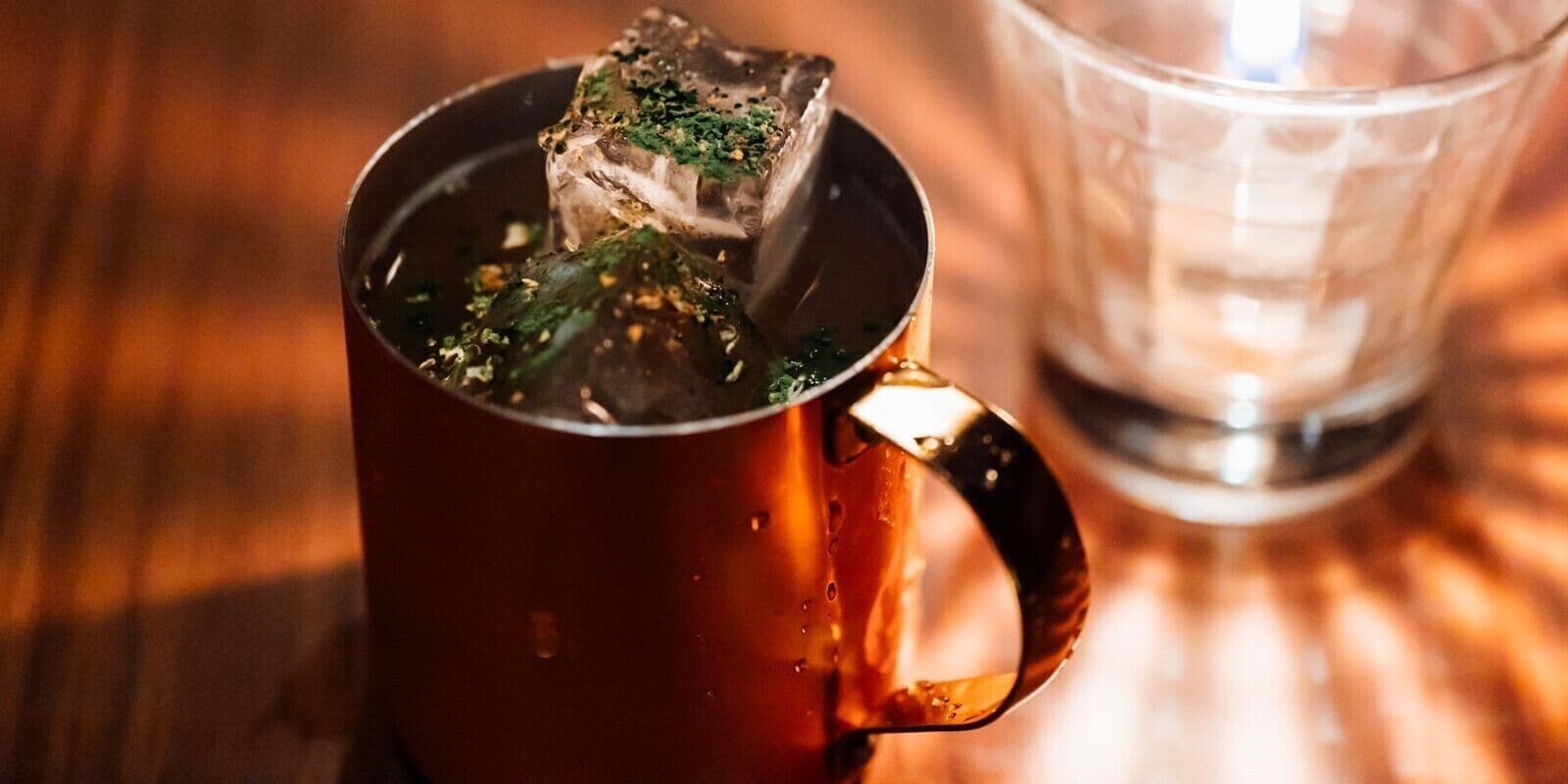 A mug with a tea bag and a glass of water on a wooden surface.