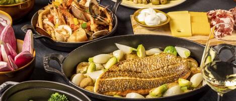 Una variedad de platos de mariscos, incluyendo un pescado entero en una sartén, almejas y una ensalada con aceitunas y tomates.