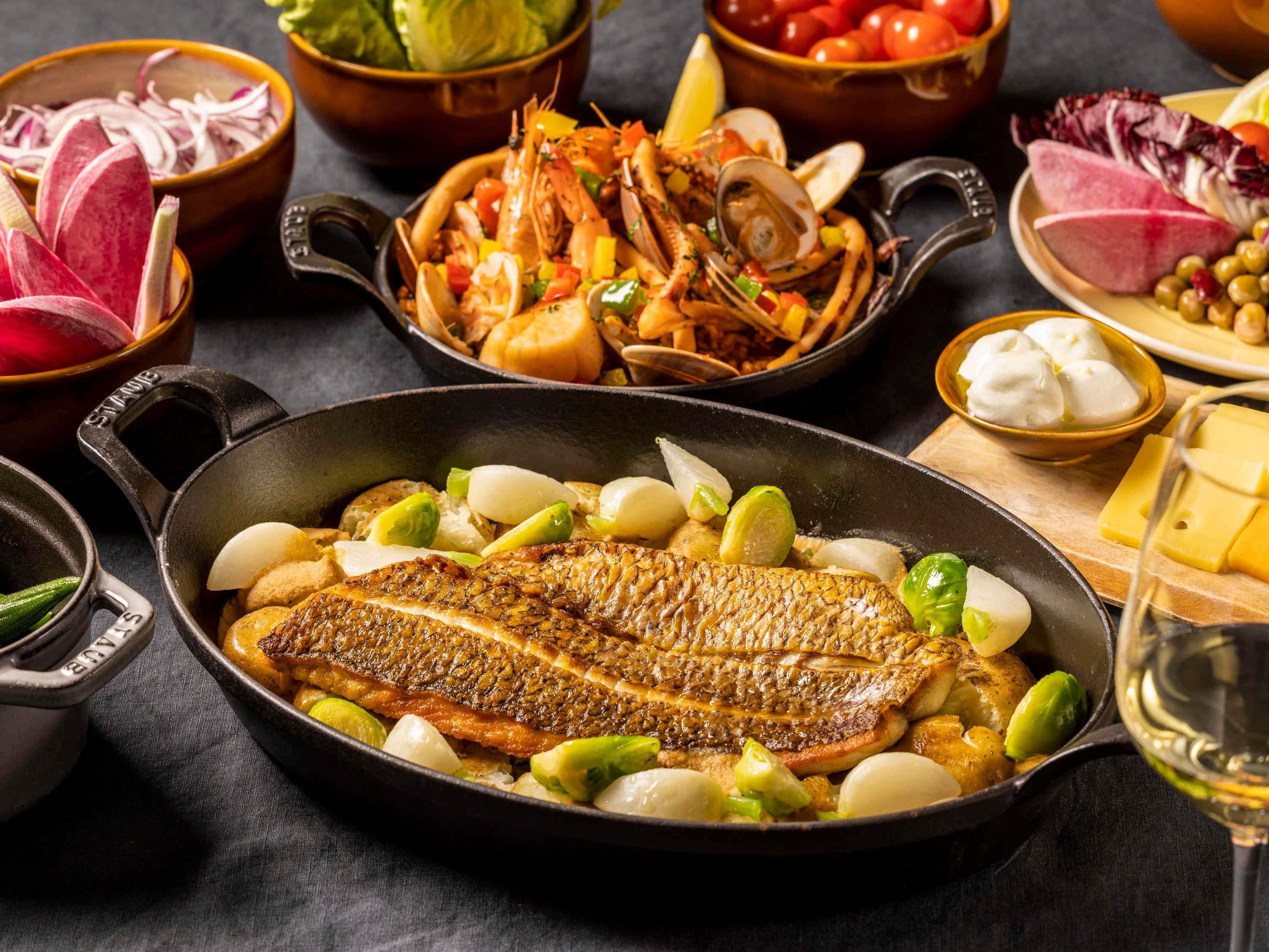 Un assortiment de plats comprenant un poisson entier grillé, des légumes et des fruits de mer.