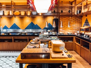 A kitchen with a long counter, various cooking utensils, and a large block of cheese. - Mercure Hida Takayama (Takayama)