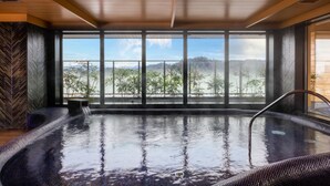 A hot tub with a view of mountains and trees through large windows. - Mercure Hida Takayama (Takayama)