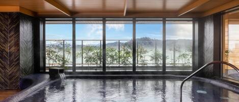 Un jacuzzi con vistas a montañas y árboles a través de amplios ventanales.