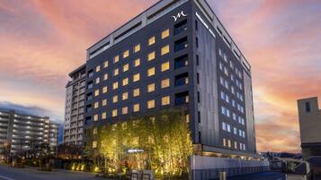 A modern hotel building with multiple floors, a prominent entrance with illuminated signage, and a well-lit facade.