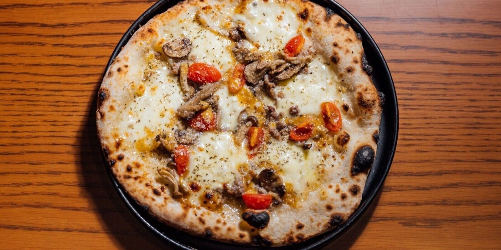 A pizza with toppings on a black skillet on a wooden table.