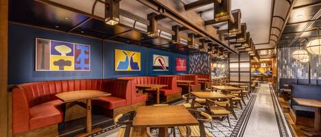 Un restaurante con asientos tapizados en rojo y mesas de madera, que presenta obras de arte abstracto en las paredes.