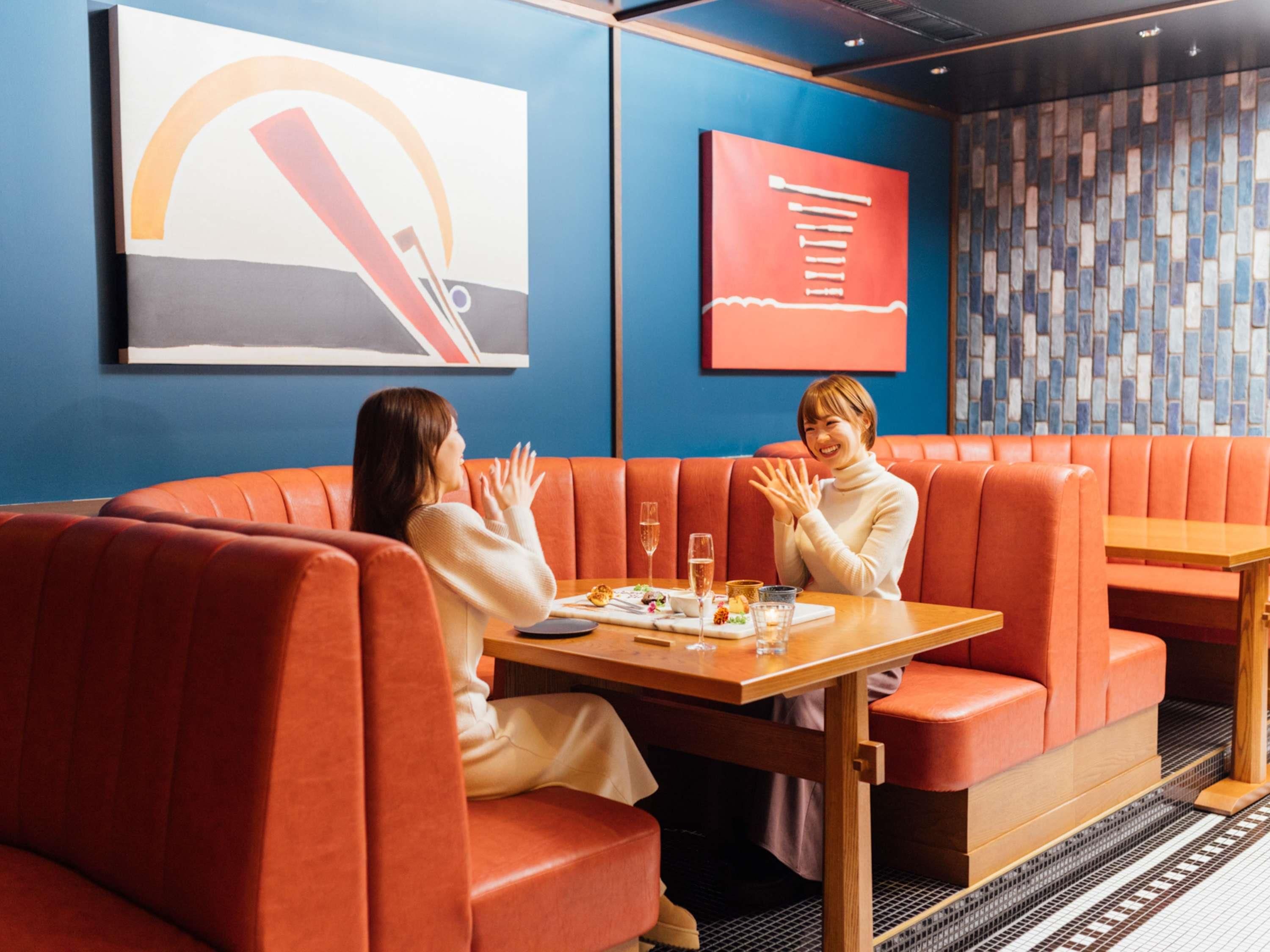 Un interior moderno con asientos rojos, una mesa con vasos y un plato, y dos personas sentadas.