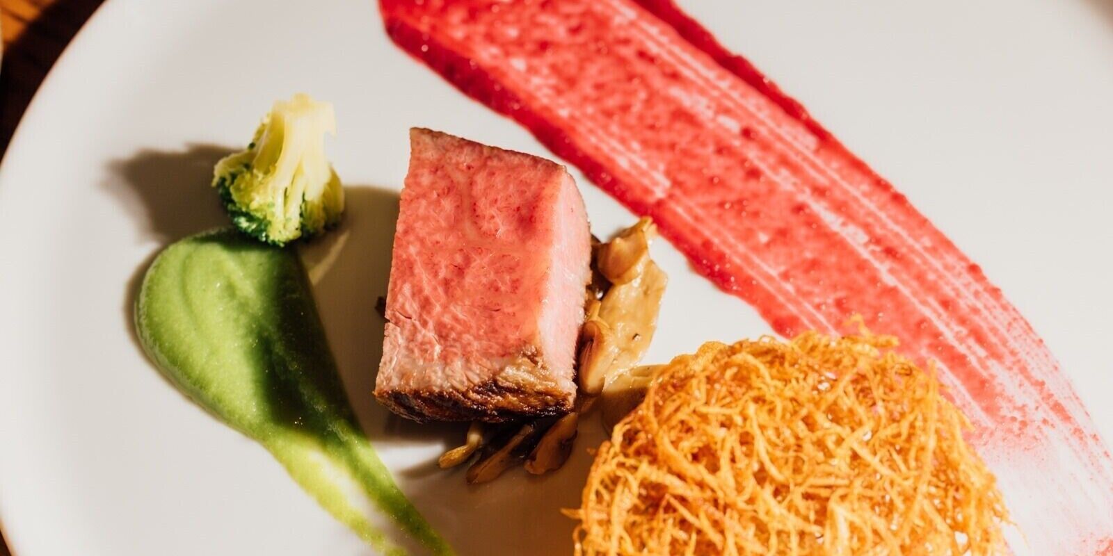 A plate with a slice of meat, a green vegetable, and a red sauce.