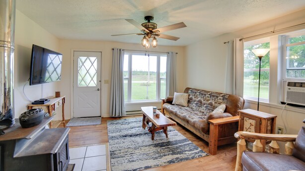 A living room with a ceiling fan, a television, a sofa, a coffee table, and a fireplace. - Pet-Friendly & Peaceful Northern Michigan Gem (Newberry)