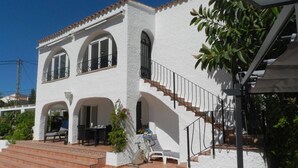 A two-story building with a white exterior, a staircase with a metal railing, and a patio area with a table and chairs. - Villa Tina para 8 personas (Calpe)