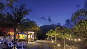 Un restaurante con terraza, palmeras y una montaña al fondo.