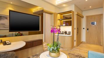 A modern hotel lobby with a large flat-screen TV, a reception desk, a seating area, and a reception counter.