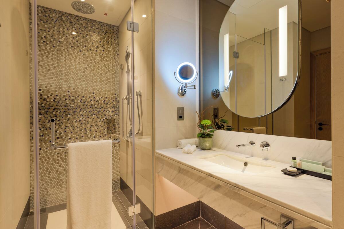 A modern bathroom with a glass shower enclosure, a large mirror, and a marble countertop.