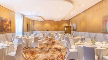 A large banquet hall with round tables set for dining, white chairs, and a marble floor.