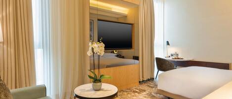 Habitación de hotel con cama, escritorio, silla, mesa redonda con planta y televisor.