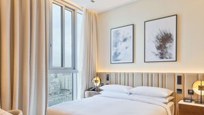 Una habitación de hotel moderna con una cama grande, una mesita de noche con lámpara y vistas a la ciudad por la ventana.