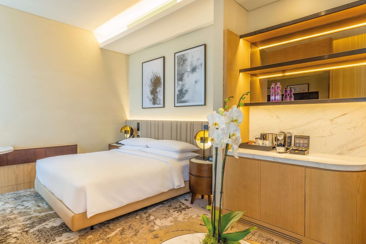 A hotel room with a bed, bedside tables, a small desk, a mirror, and a potted orchid.