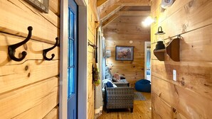 A narrow wooden hallway with a blue door, a wicker sofa, and a blue bean bag. - Cozy Blue Skies Cabin - walk to Chimney Rock & Lake Lure (Lake Lure)