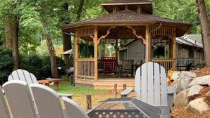 A gazebo with a wooden deck, surrounded by Adirondack chairs and a picnic table. - Cozy Blue Skies Cabin - walk to Chimney Rock & Lake Lure (Lake Lure)