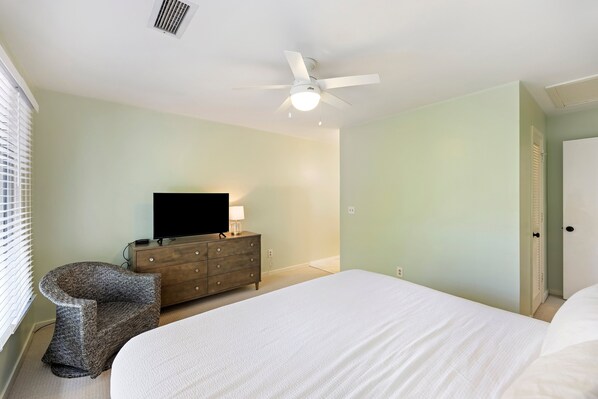 A bedroom with a bed, a dresser, a television, and a ceiling fan.