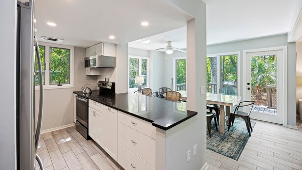 A modern kitchen with white cabinets, a black countertop, and a dining area with a table and chairs. - PET FRIENDLY Fairway Oaks Villa! Kiawah West Beach (Kiawah Island)